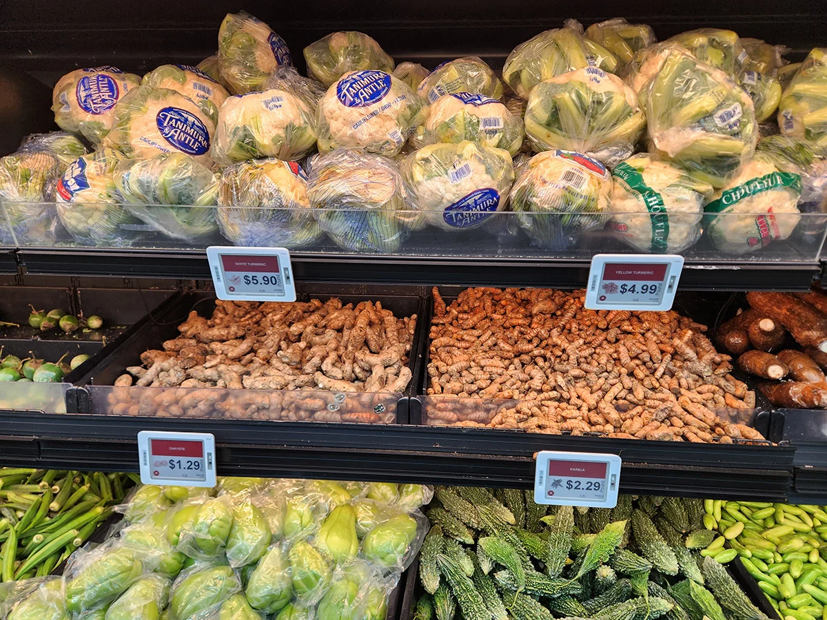 Fresh produce aisle showing cauliflower, ginger, turmeric, and green vegetables